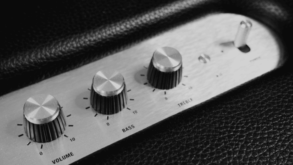 Black and white image of an amplifier's control panel, showing three knobs against a textured black background. From left to right, the labelled knobs are for volume, bass, and treble.