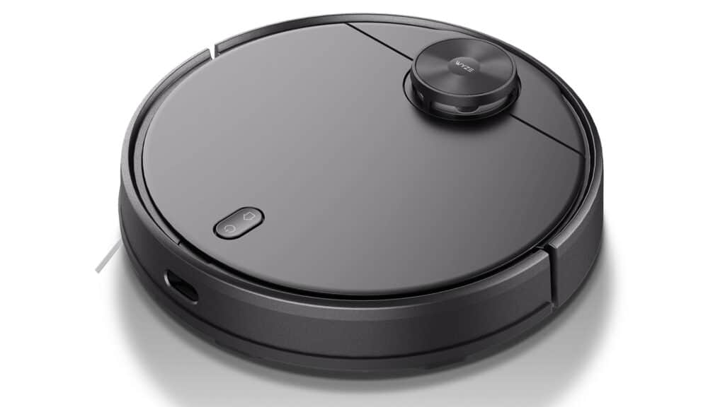 A Wyze robot vacuum cleaner displayed against a white background. It has a sleek, circular black design with a prominent 'Wyze' logo on top. Two buttons for power and navigation are visible on the surface, and a small bumper and a sensor can be seen on the front part of the vacuum.