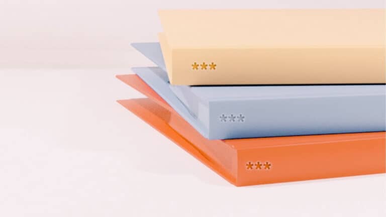 A stack of hardcover books in pastel colors, arranged in descending order with the largest at the bottom. The visible book spines are peach, light blue, and cream, each featuring a unique star symbol design. The soft color palette gives a calm and orderly impression.